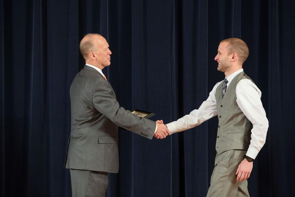 Doctor Potteiger shaking hands with an award recipient in a grey tuxedo vest
